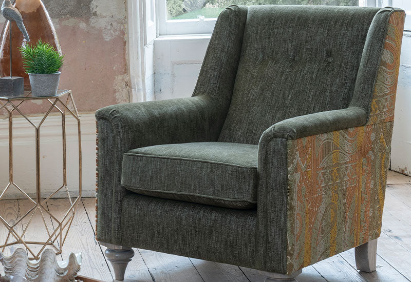 Green armchair with patterned side in a room with a small table and plant.