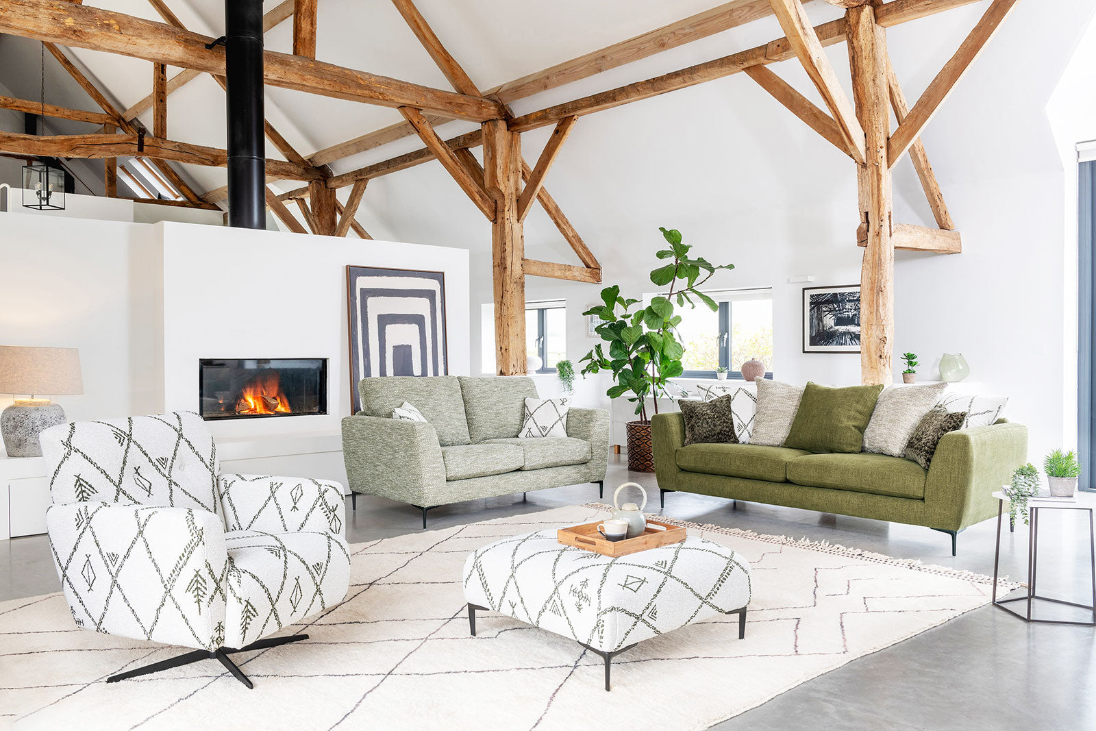 Inka dark green 3 seater sofa, light green two seater sofa, white swivel armchair patterned with diagonal green natural images and matching footstool. Sofa range set in a contemporary living room with grey floor, white rug and natural wooden rafters.