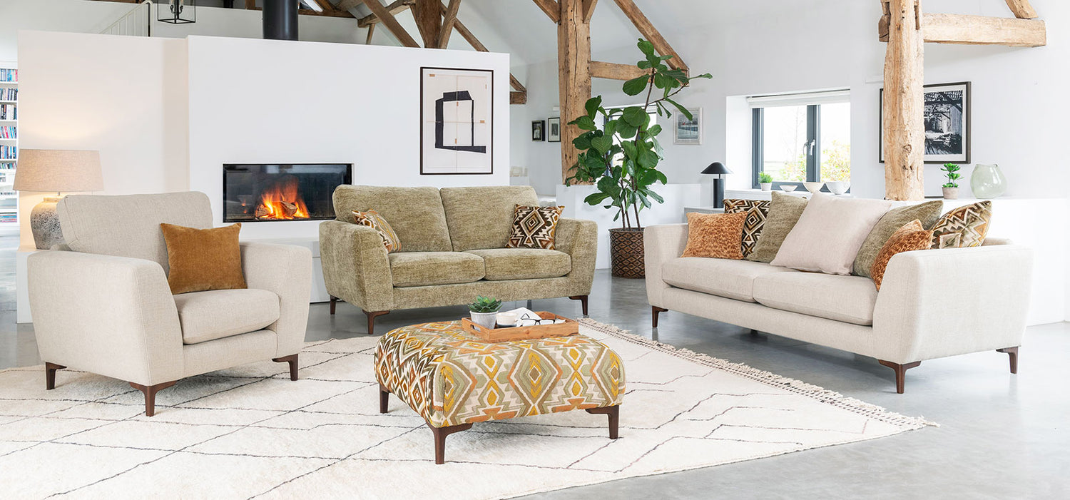 Living room with beige sofa, armchair, and ottoman with a fireplace in the background.