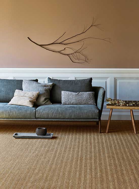A brown sisal carpet in a room with a blue sofa and brown wall